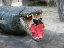 Child reading a book inside the mouth of a fake crocodile