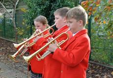 three children playing the trumpet outside