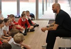 children sitting on the floor in a hall listening to a poet talking