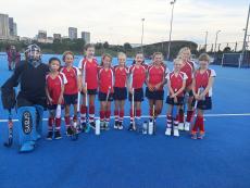 hockey girls team standing on an astro pitch posing for a photo