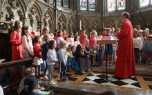 Children standing in rows in a chapel singing facing a choir master