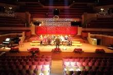 the inside of a concert hall looking down towards the stage where a choir is reshearsing