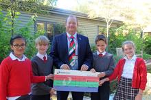 Two children standing to the left and two children standing to the right of a man holding a large charity presentation cheque