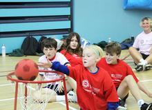 Children in a gymnasium sitting on the floor playing floor basketball