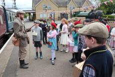 children dressed as wartime evacuees standing next to a train at a station