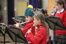Children standing in front of music stands playing wind instruments wearing Christmas attire