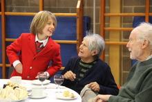 A child greeting two elderly visitors who are seated at a table