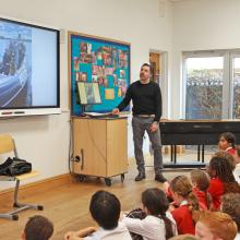 man talking by an interactive board with children in front