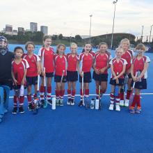 hockey girls team standing on an astro pitch posing for a photo