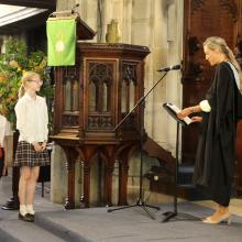 children in a church with a head teacher reading from a lecturn