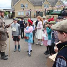 children dressed as wartime evacuees standing next to a train at a station