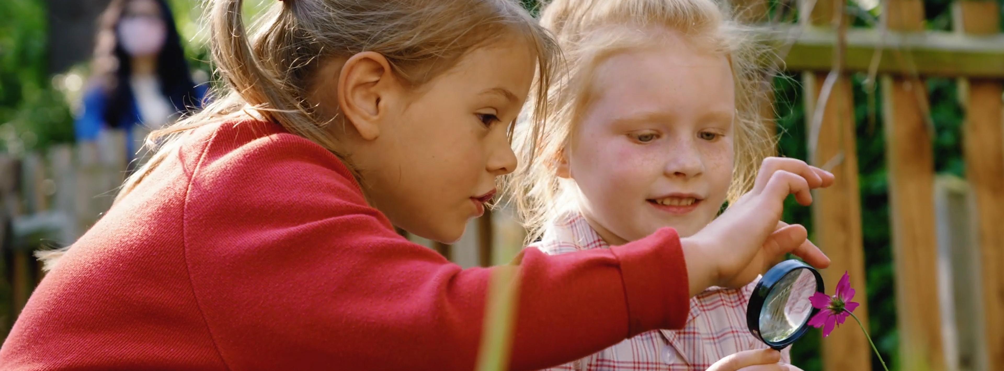 two girls looking at a flower through a magnifying glass